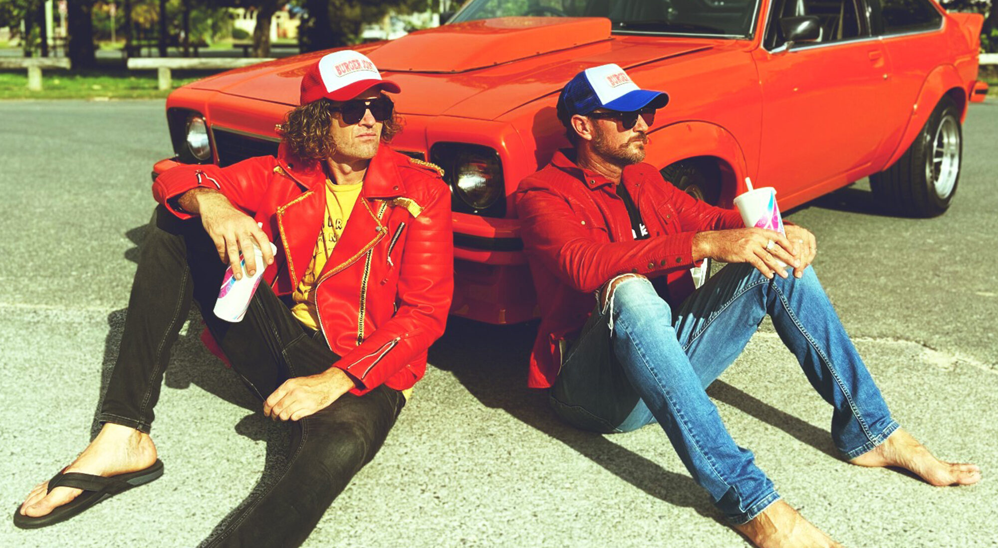 Two people sat in front of an old classic red car.