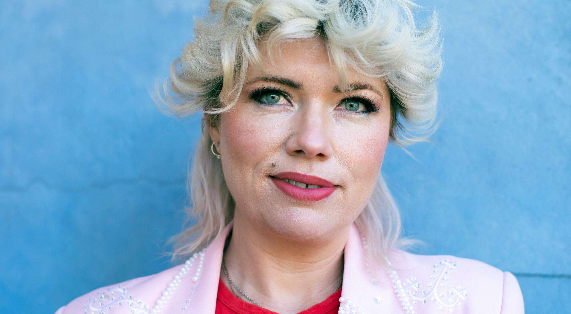 Portrait of a person with a mullet stood in front of a blue background.