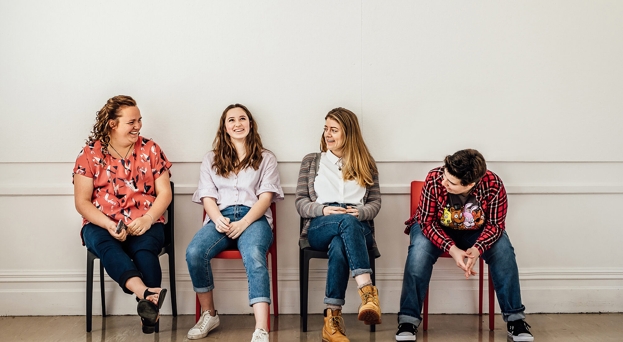 People sat on chairs against a white wall. They are talking.